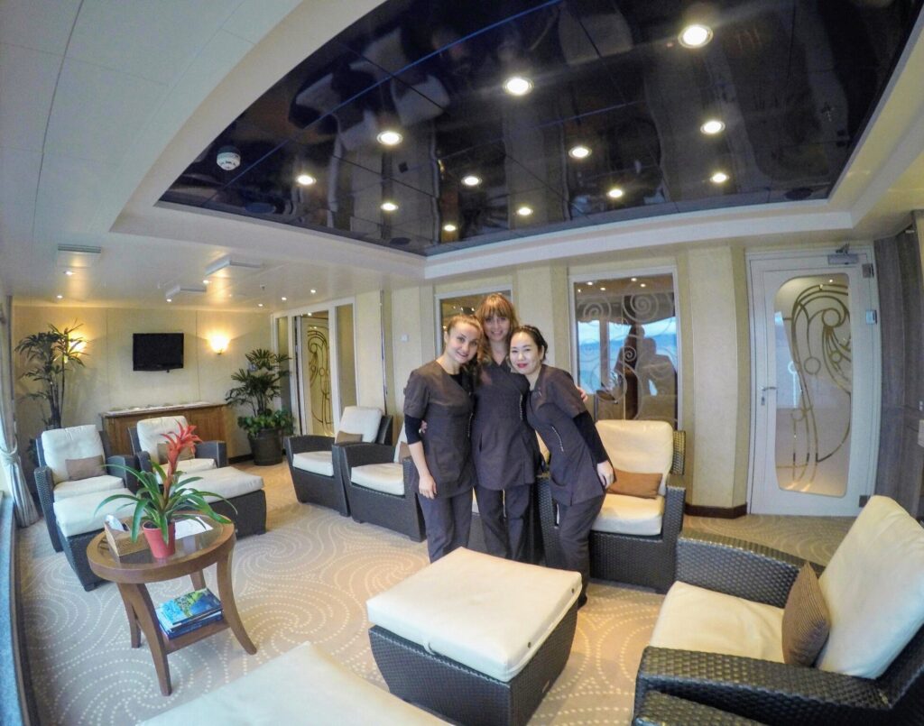 Three women in uniform posing on a ship, smiling in a relaxing lounge area.