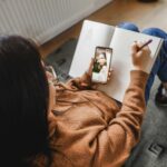 Woman looking at her phone for hairstyle inspiration, jotting down ideas in a notebook