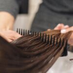 Close-up of a stylist examining the condition of a client’s hair with a comb.